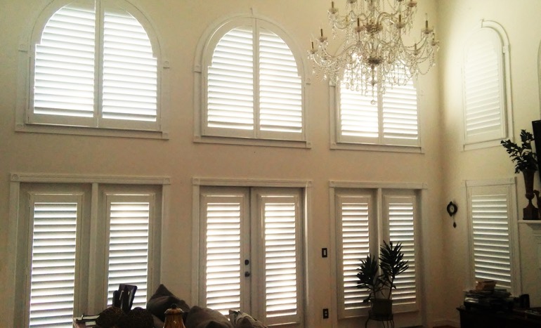 Entertainment room in open concept San Diego house with plantation shutters on arch windows.