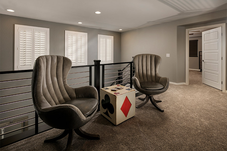 A white window treatment on a darker wall can do wonders for your San Diego home. two chairs and a small dice-themed table in front of a stairwell with shuttered covered small windows