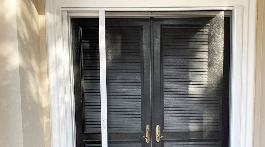 A dark retractable screen pulled partially in front of a home's black double door.