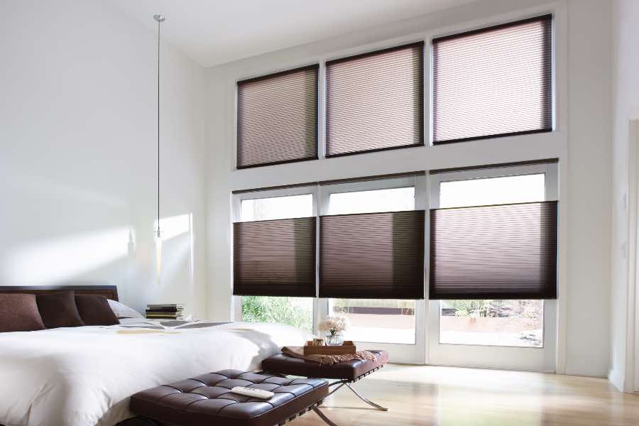 Cordless cellular shades add to the sleek, modern appearance of this bedroom. Motorized functionality works well with hard-to-reach windows. Top-down, bottom-up cellular shades covering windows in stylish bedroom