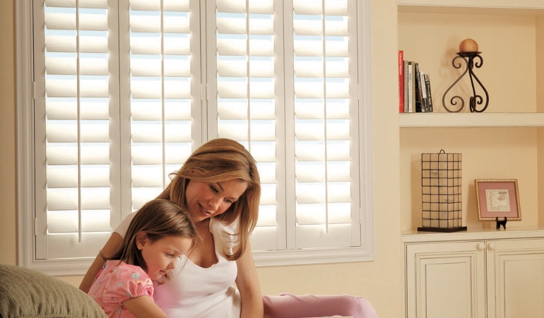 Easy to clean faux wood shutters are great cord-free options for kids. Mom and daughter in front of window
