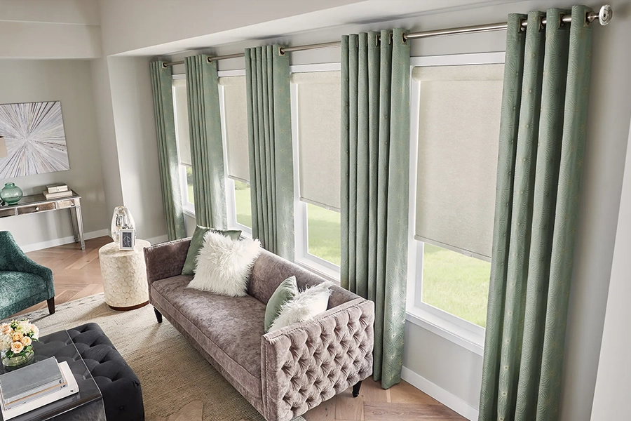Sage green draperies overlaying cream colored roller shades in a large living room