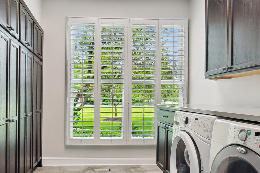 Find the perfect level of natural light for your San Diego laundry room with interior shutters. White Polywood shutters letting light through a laundry room window