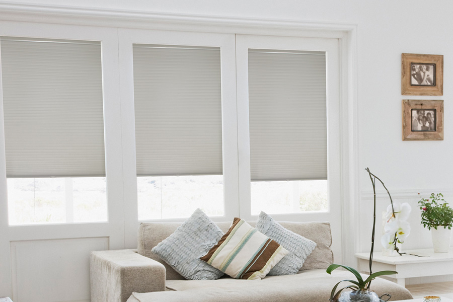 Cellular shades help insulate your windows during the cold season. Light gray cellular shades inside a white and rustic styled living room.